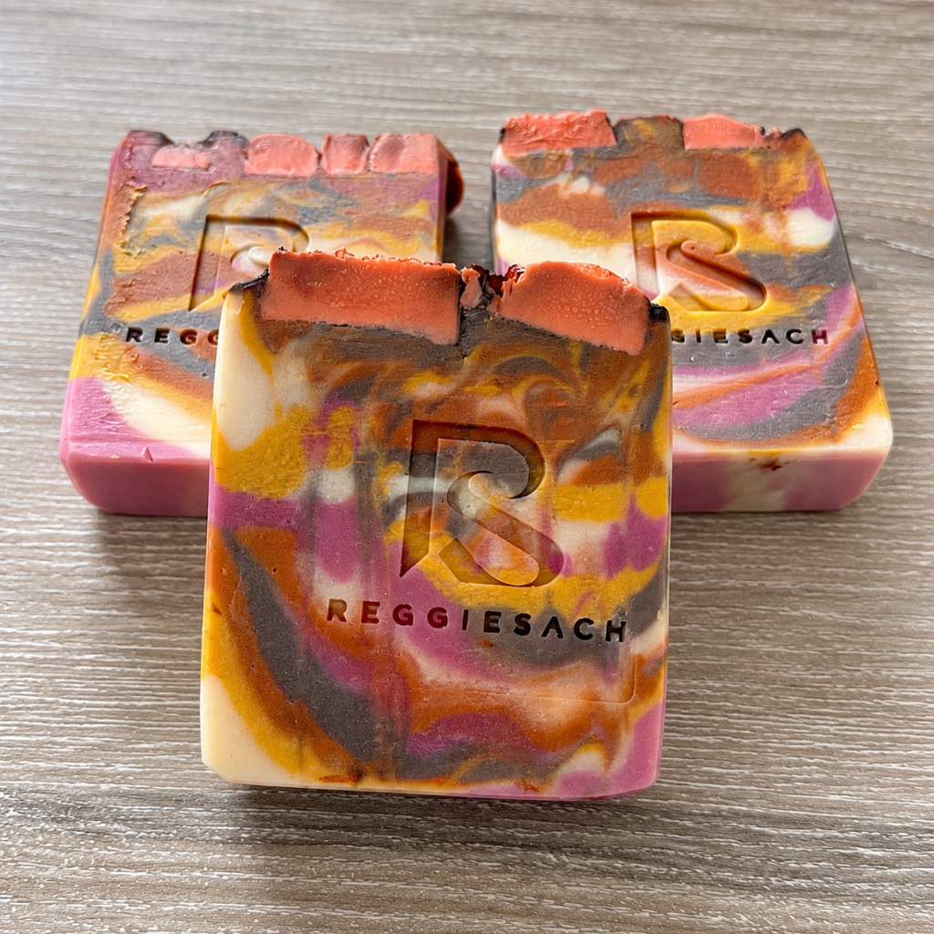 ReggieSach Harvest Sunset Bar Soap trio on light wood grain, pink, purple and mustard marbled swirls with embossed R logo