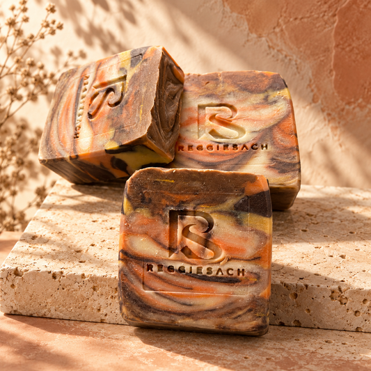 ReggieSach Pumpkin Pickin' Bar Soap trio on a tan stone plinth beside dried flowers in warm autumn light