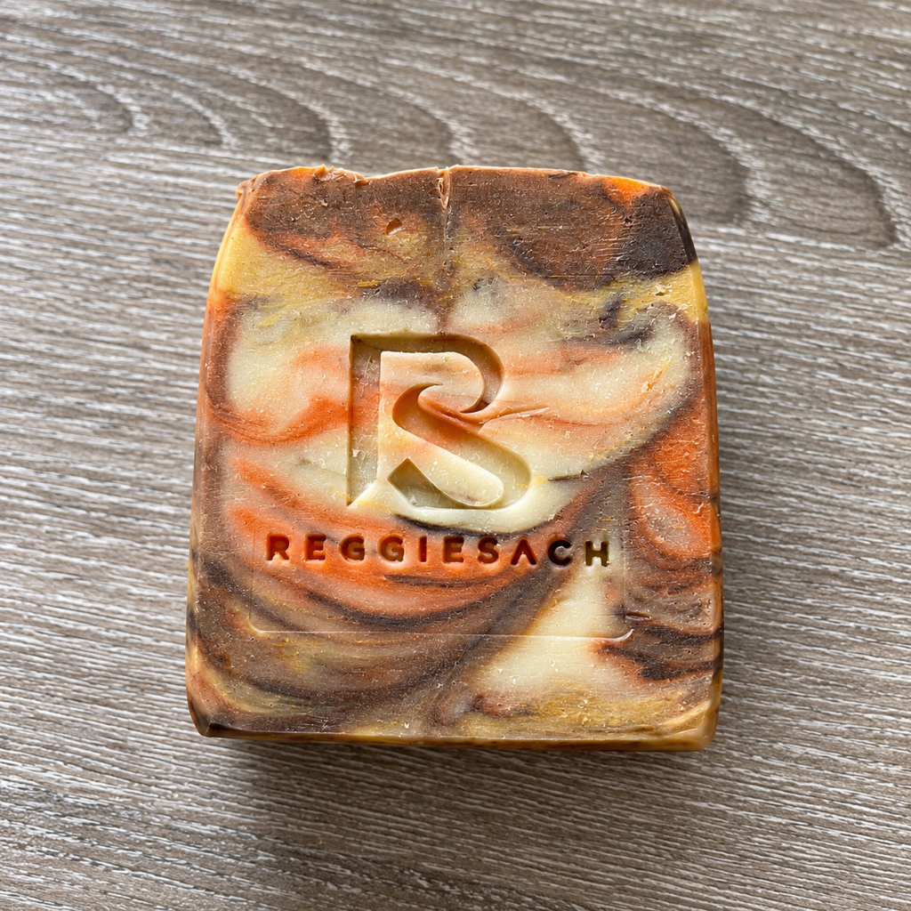 ReggieSach Pumpkin Pickin' Bar Soap, a single marbled bar in burnt orange and cream swirls with stamped ReggieSach R logo on a stone surface
