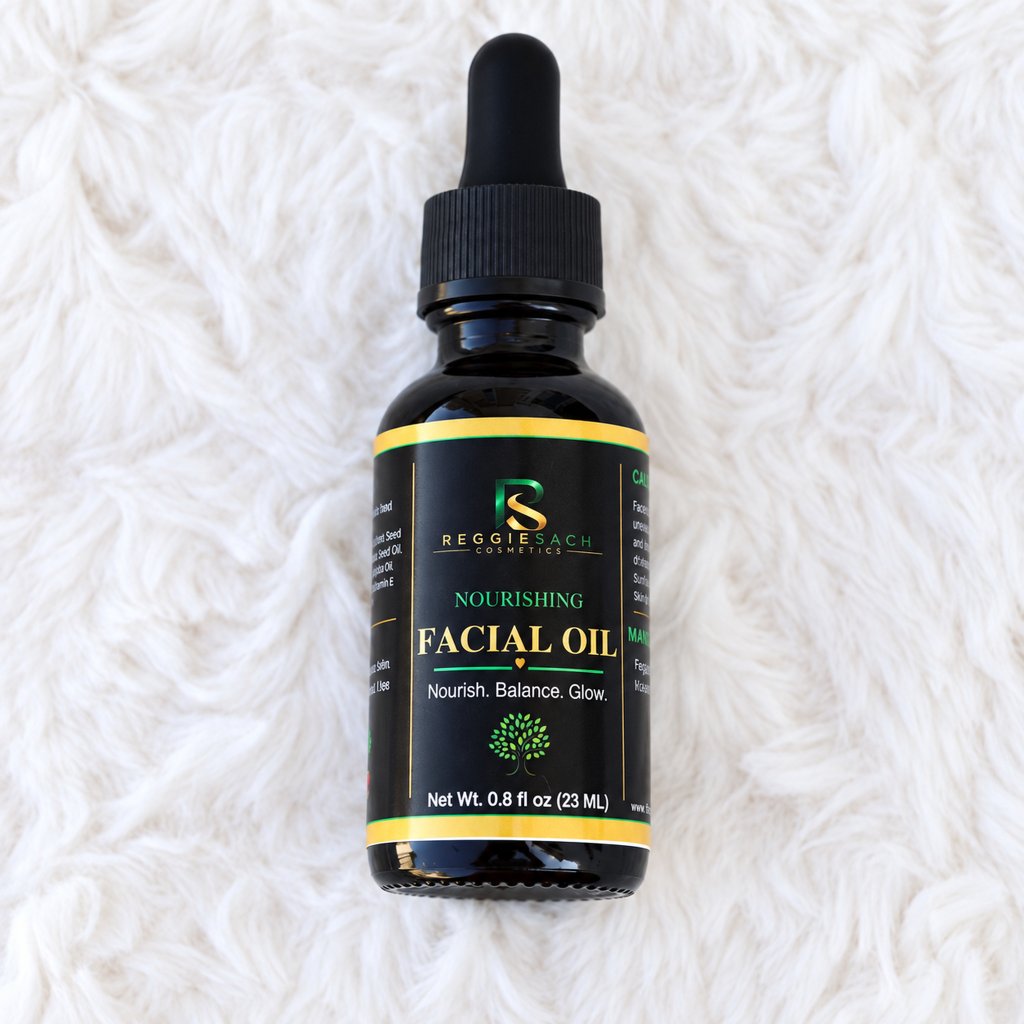 ReggieSach Cosmetics Facial Oil in a 1 oz glass dropper bottle with gold cap, on a soft white blanket.