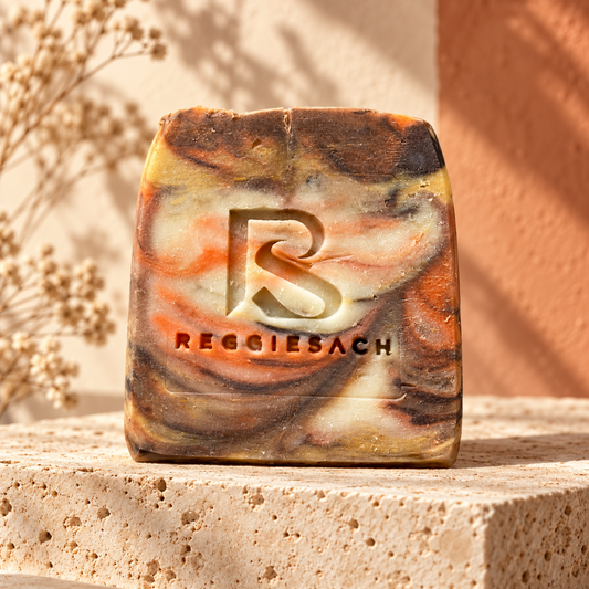 ReggieSach Pumpkin Pickin' Bar Soap, a single marbled bar in burnt orange and cream on travertine with baby's breath flowers