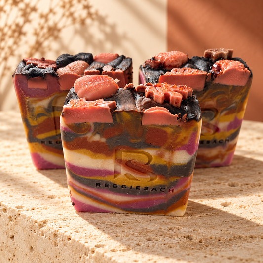 ReggieSach Harvest Sunset Bar Soap, three marbled bars in pink, purple and mustard swirls on travertine stone with embossed ReggieSach logo, warm sunlight and dried botanicals