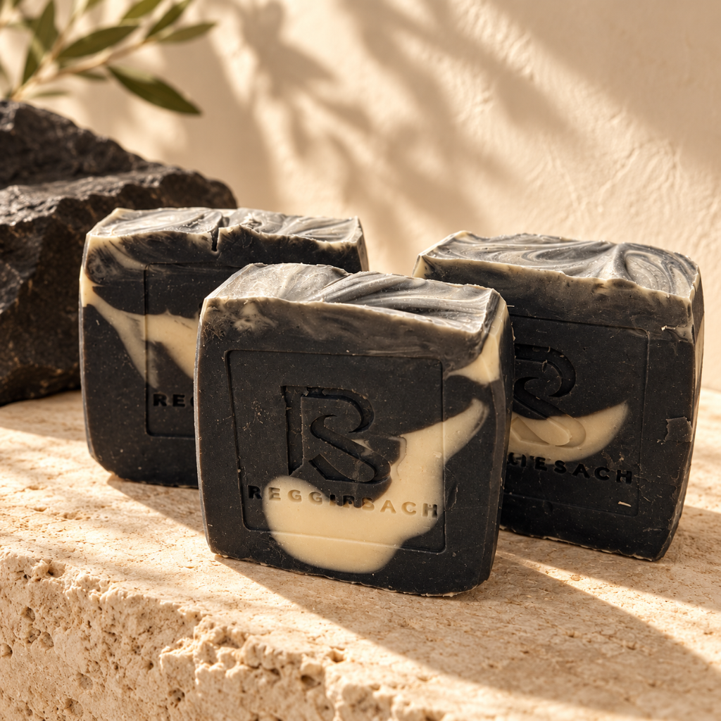 ReggieSach Spooky Vanilla Bar Soap bars on travertine stone in soft sunlight, charcoal black and cream swirls
