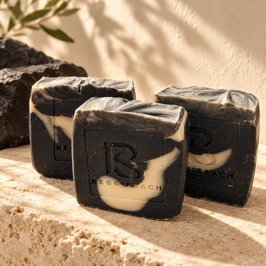 ReggieSach Spooky Vanilla Bar Soap bars on travertine stone in soft sunlight, charcoal black and cream swirls